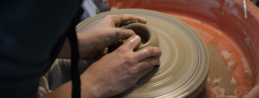 hands stretching a clay product on a pottery wheel